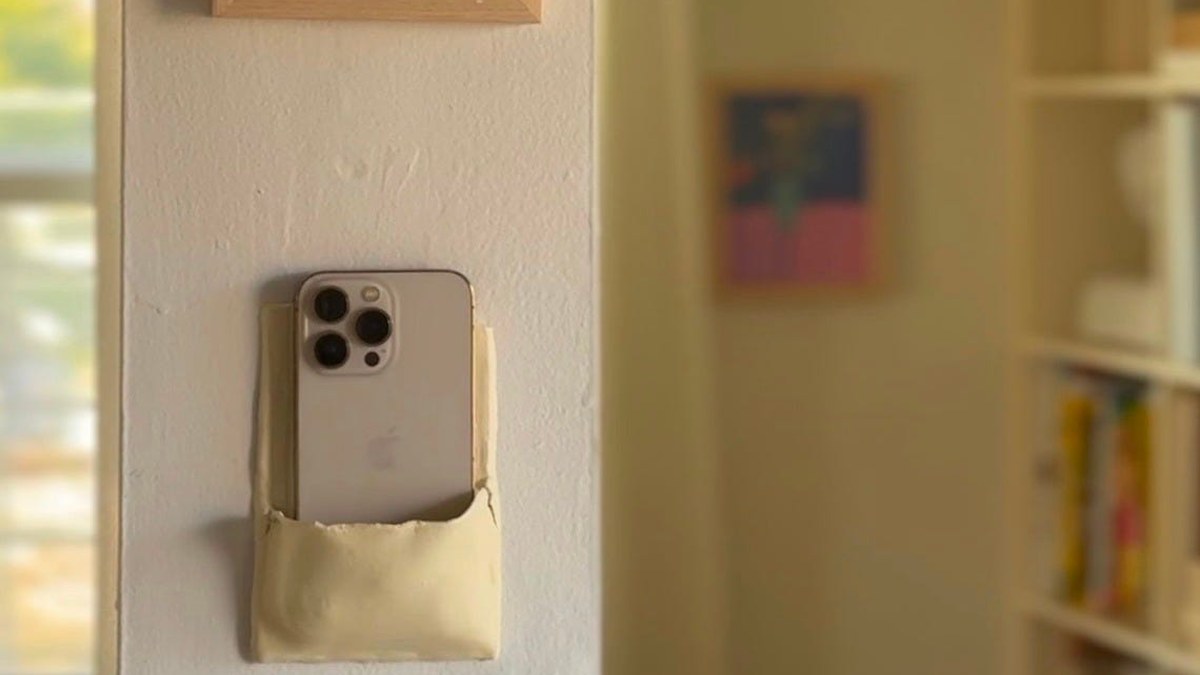 A smartphone tucked into a small pocket carved into a wall, kept at a deliberate distance.